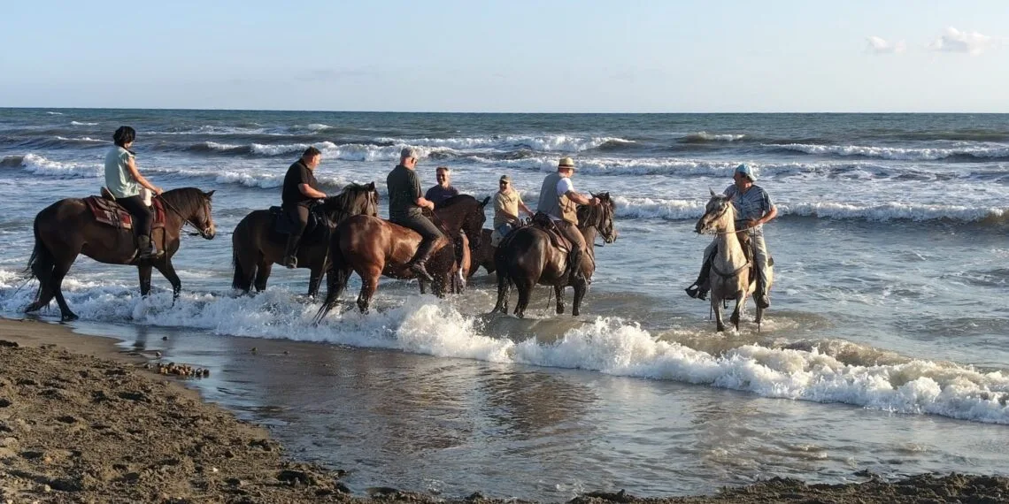 Cavalieri e cavalli entrano in acqua tra le onde del mare, all'arrivo della traversata Da Costa a Costa