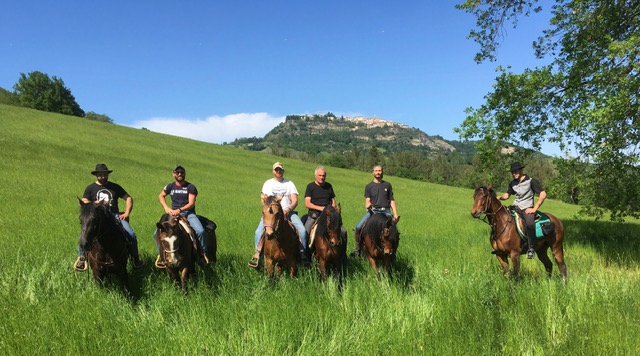 Cavalieri tra l'erba alta con un borgo collinare sullo sfondo